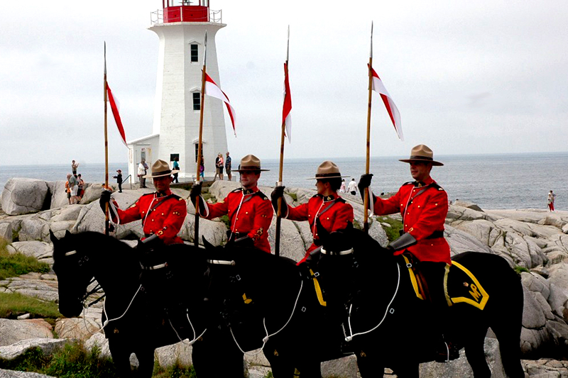 Four mounties atop their steeds in front of a lighthouse