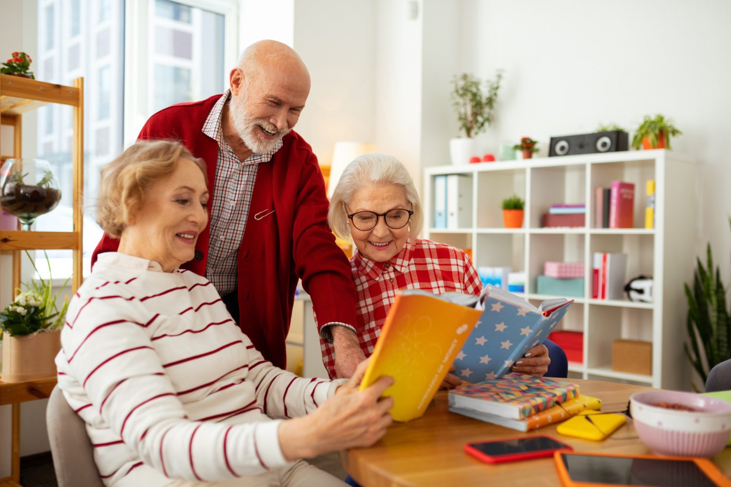 look-here-joyful-senior-women-smiling-while-showing-books-their-friend